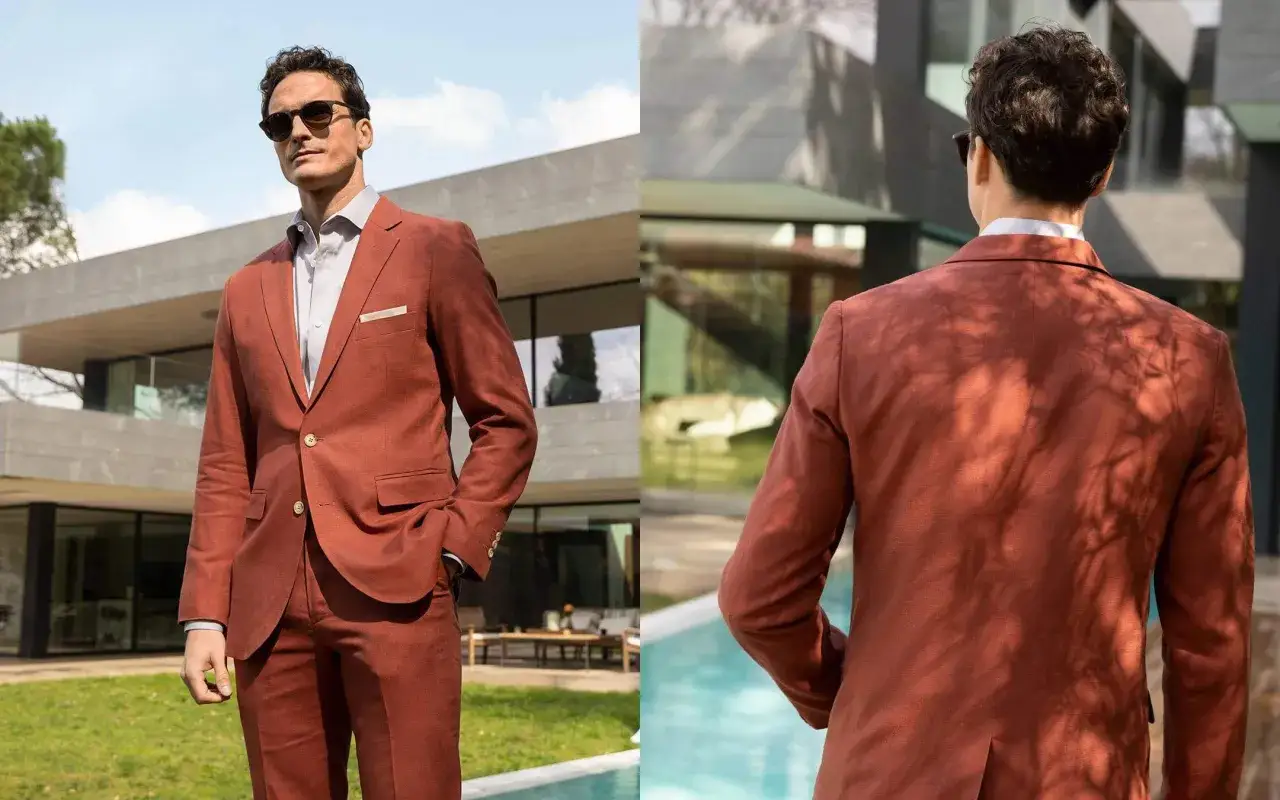 Mann in einem rostbraunen, semi-formellen Anzug mit Sonnenbrille, l&auml;ssig vor einer modernen Villa stehend.