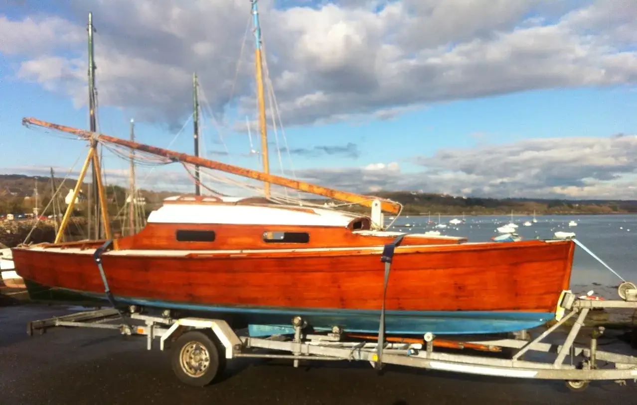 Bateau en bois verni, prêt à naviguer. Ce belouga bateau attend son heure sur sa remorque, face à une baie paisible.