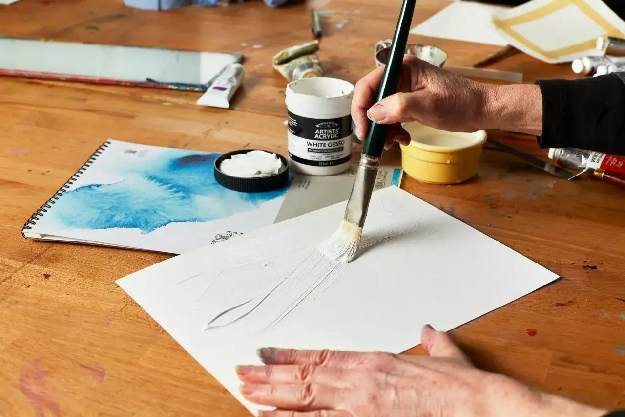 Une main applique du blanc de titane sur une feuille, préparant une toile pour une peinture acrylique.