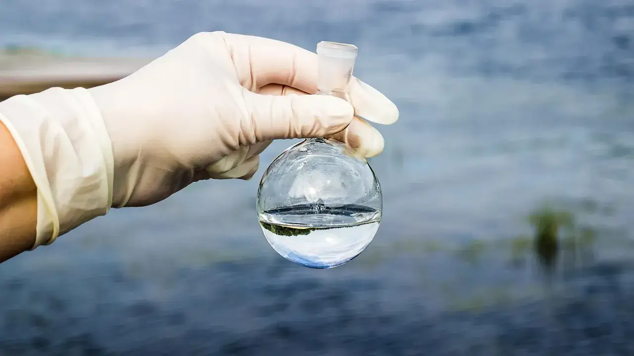 Main tenant une fiole d'eau, une main gantée examine le liquide, craignant la présence de poison dans l'eau.