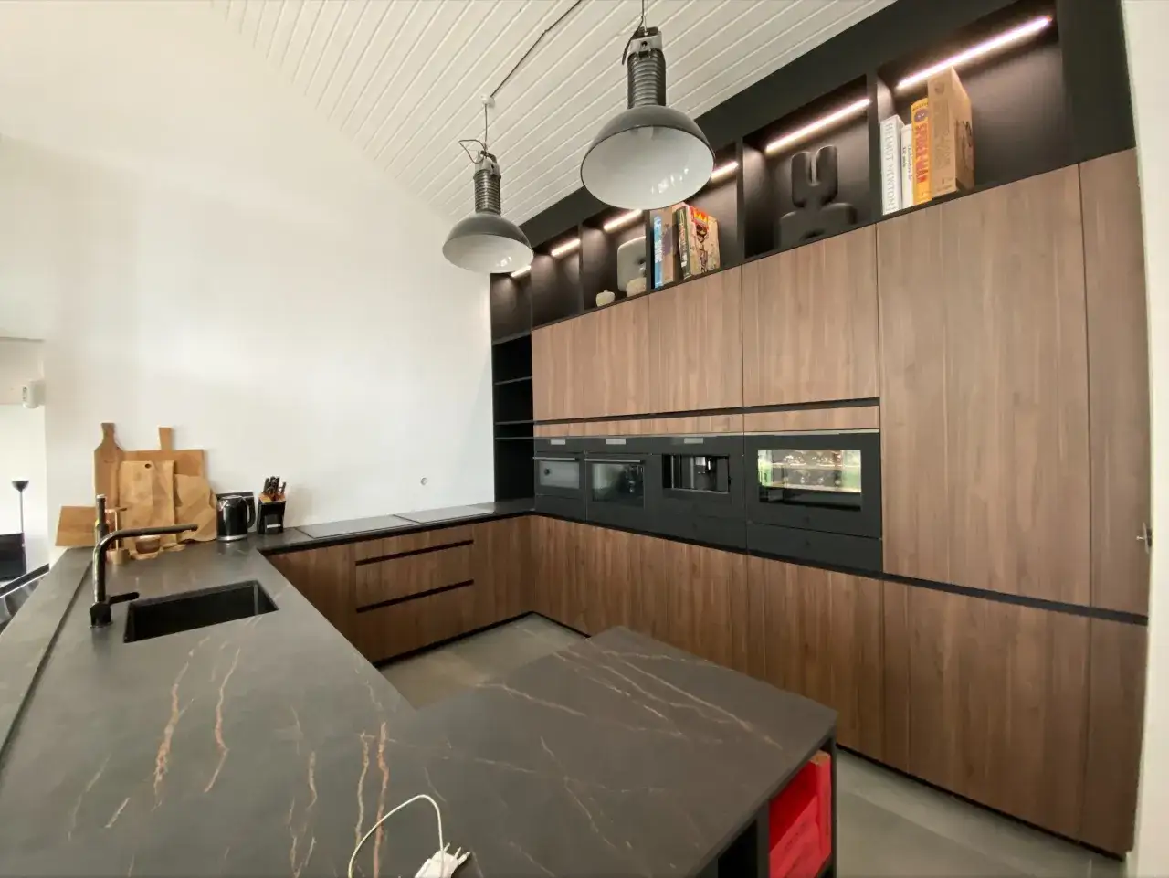 Plan cuisine moderne avec îlot central, plan de travail en marbre noir veiné, meubles en bois, électroménagers intégrés et éclairage d'ambiance.