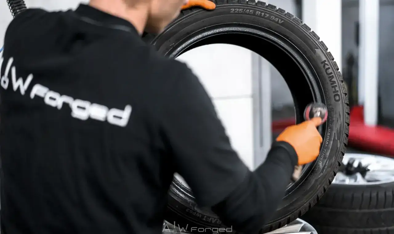 Mechanik w pomarańczowych rękawiczkach czyści oponę. Dowiedz się, ile kosztuje wymiana opon.