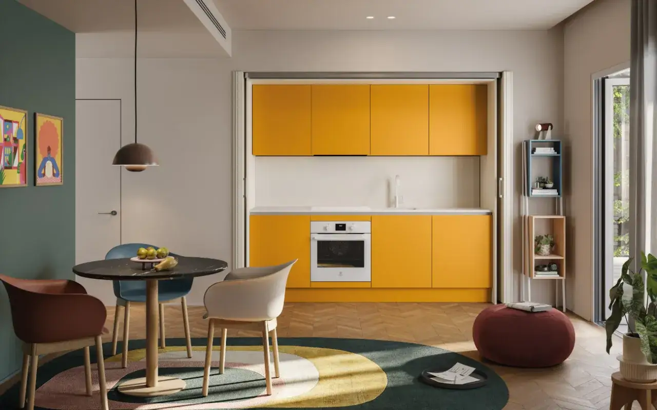 Una cucina piccola e luminosa con mobili gialli vivaci, un tavolo rotondo con sedie colorate e un tappeto circolare.