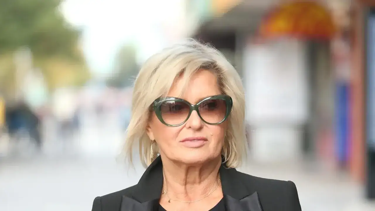 Ewa Kasprzyk w okularach przeciwsłonecznych i czarnej marynarce, z blond włosami i delikatnym makijażem.