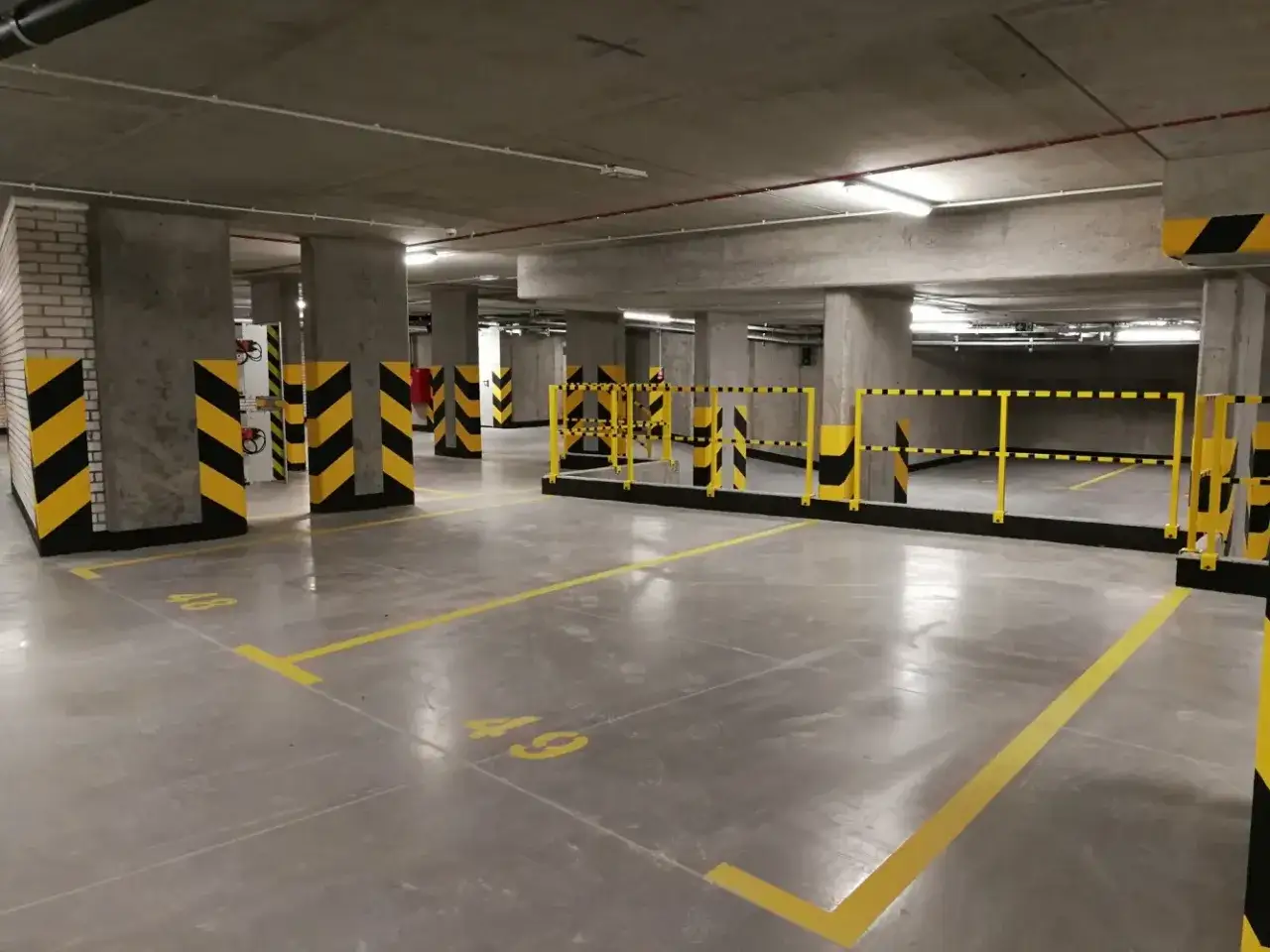 Nowe miejsce parkingowe pod blokiem, oznaczone numerami 48 i 49, z żółtymi pasami bezpieczeństwa.
