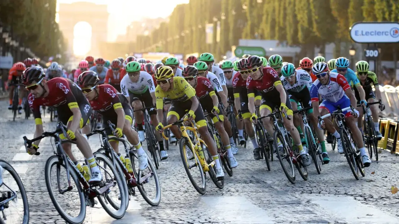 Cyclists in a peloton, likely during the Tour de France, race towards the Arc de Triomphe. Their determined faces hint at the high tour de france average speed.