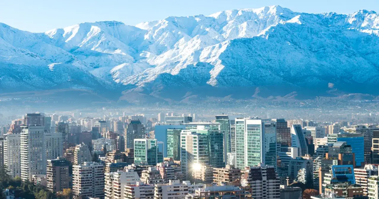 Widok na nowoczesne budynki Santiago de Chile z ośnieżonymi Andami w tle.