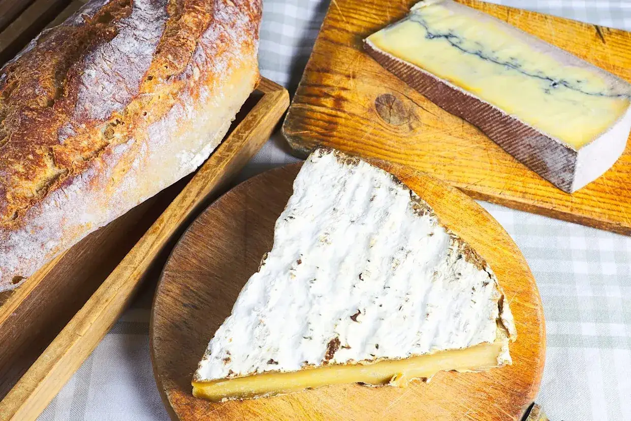 Une baguette croustillante et une part de brie de Meaux enceinte, avec un autre fromage bleu sur une planche en bois.