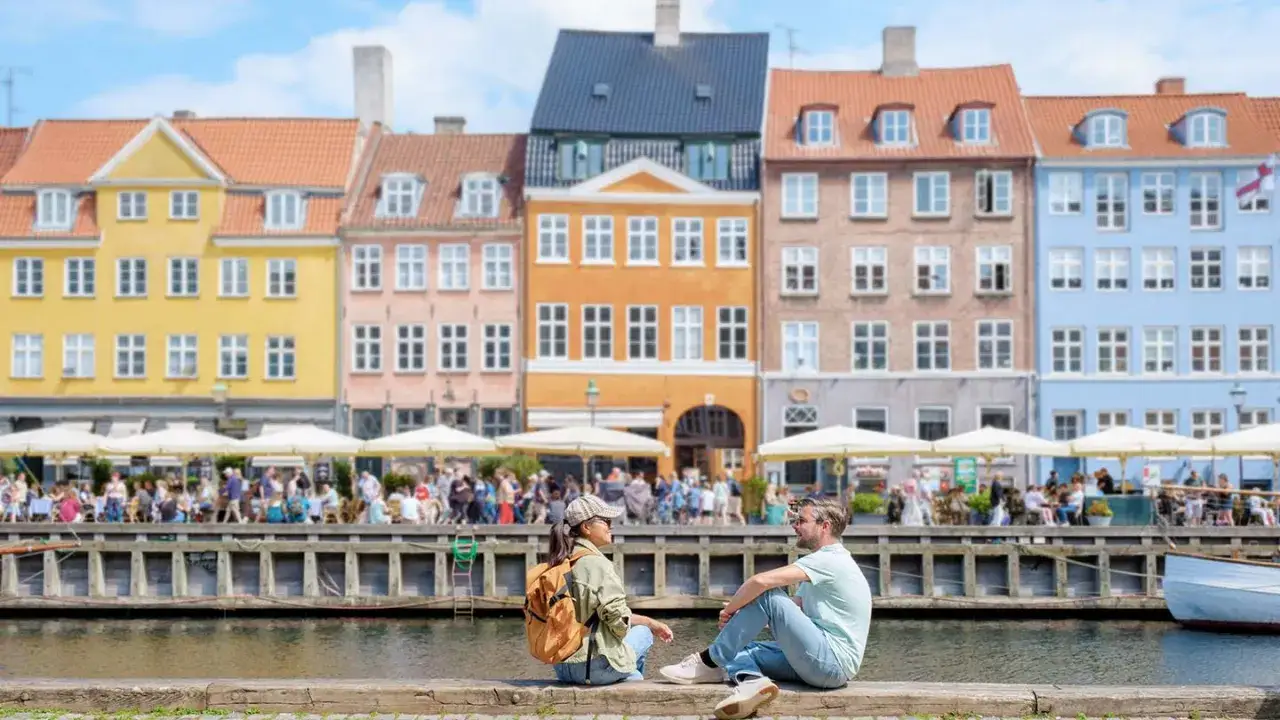Ett par njuter av utsikten &ouml;ver Nyhavn i K&ouml;penhamn, perfekt f&ouml;r weekendresor till Danmark. F&auml;rgglada hus och folkliv vid vattnet.