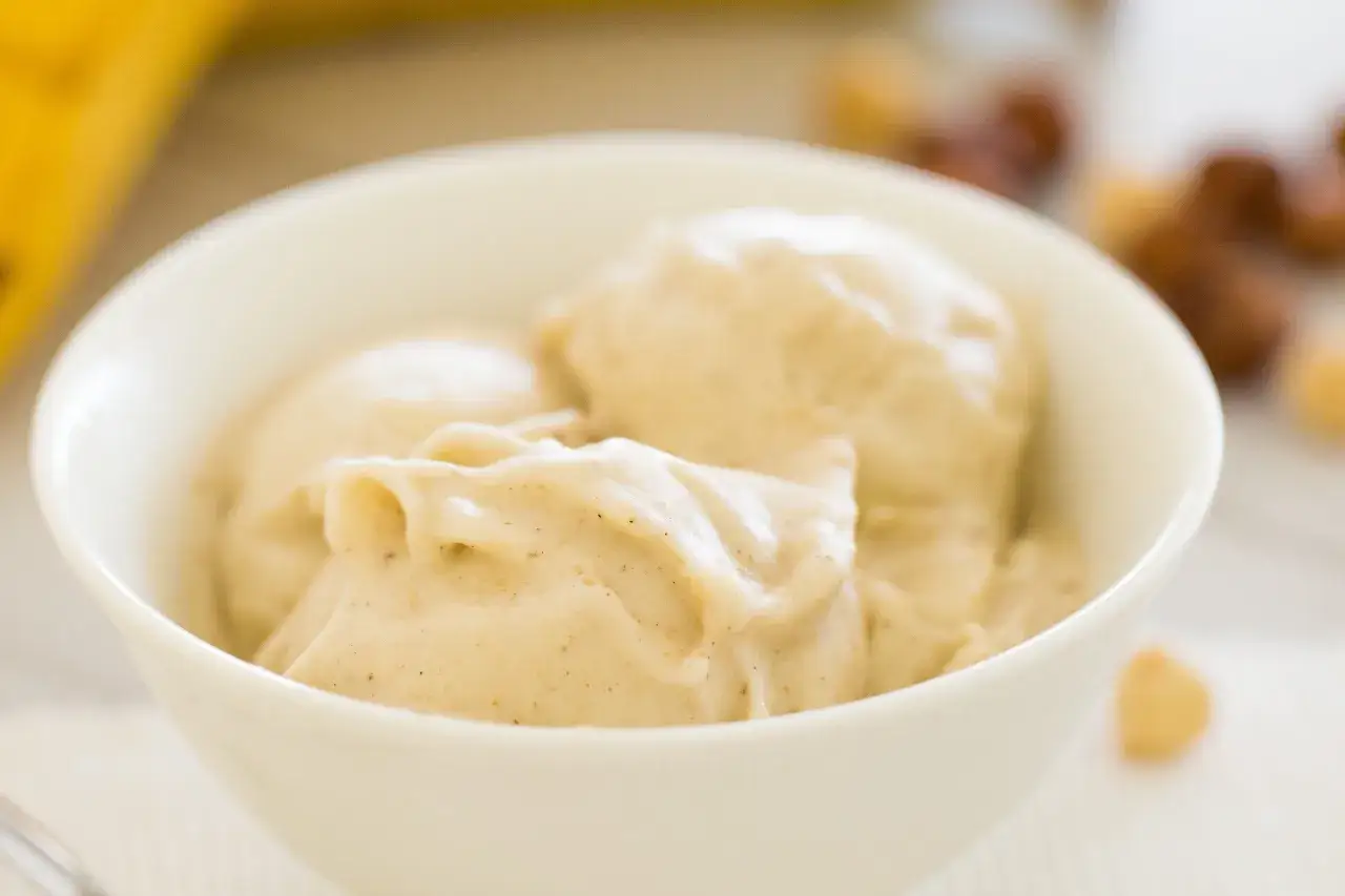 Cremiges, veganes Bananeneis in einer weißen Schüssel, garniert mit kleinen braunen Sprenkeln. Perfekt für heiße Tage!