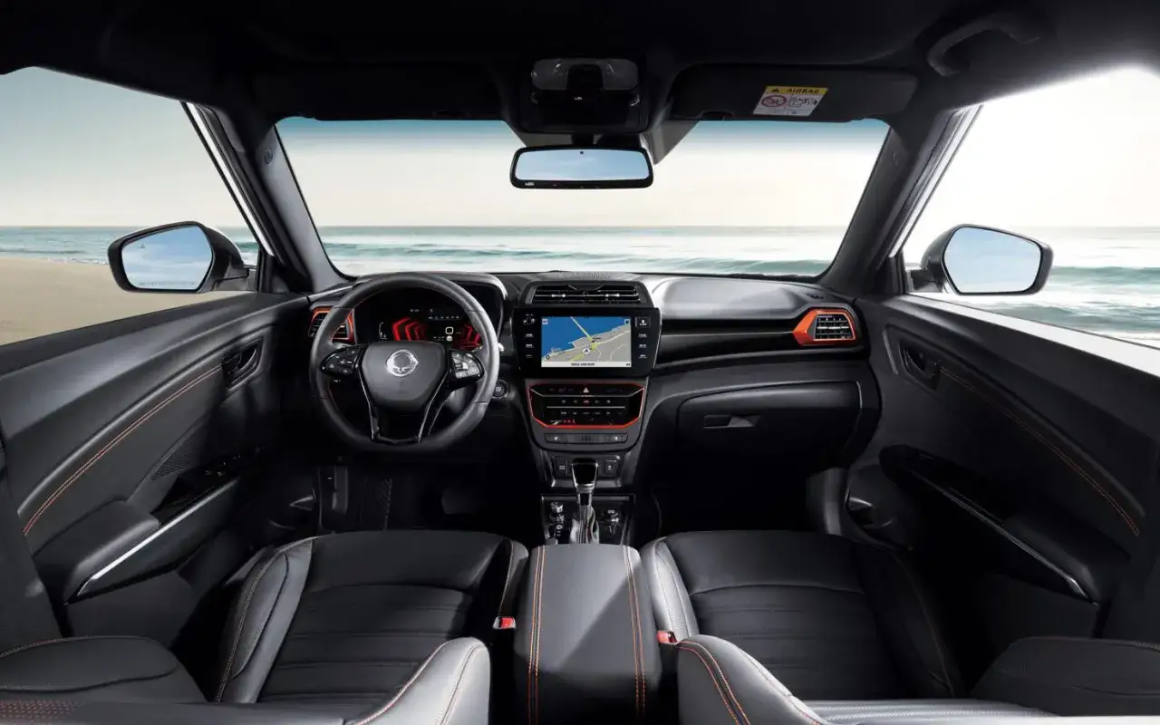 Wnętrze SsangYong Tivoli z widokiem na plażę i morze. Skórzana tapicerka z pomarańczowymi przeszyciami, nowoczesny ekran multimedialny.