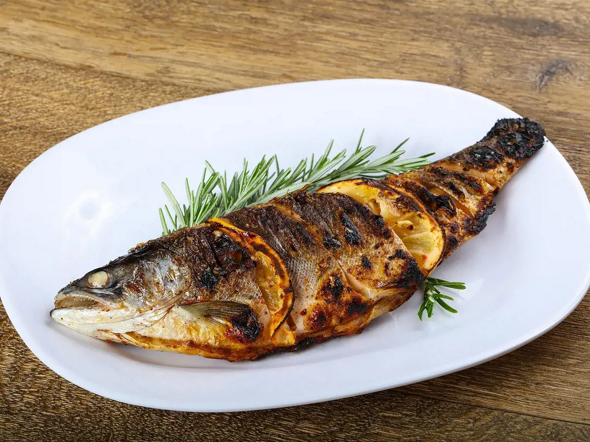 Truite enti&egrave;re grill&eacute;e au barbecue, garnie de rondelles de citron et de romarin, pr&ecirc;te &agrave; &ecirc;tre d&eacute;gust&eacute;e.