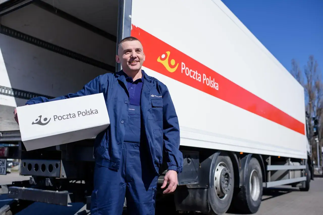 Pracownik Poczty Polskiej z paczką w ręku przy ciężarówce. Gdzie nadać mini paczkę pocztą polską? Tutaj!
