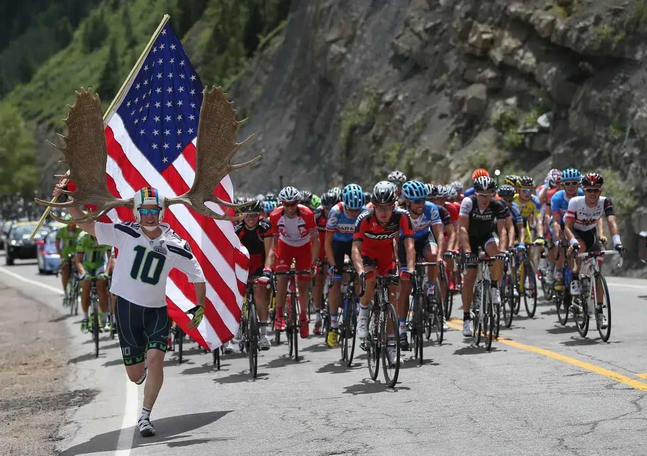 A fan with moose antlers and an American flag cheers on cyclists during the Dauphiné cycling race.