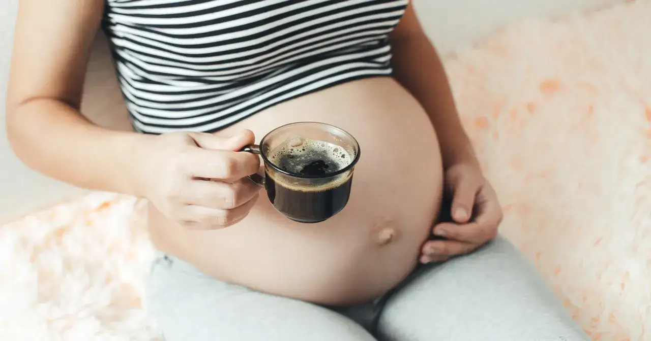 Kobieta w ciąży trzyma filiżankę kawy. Delikatny napój, który może towarzyszyć przyszłej mamie.