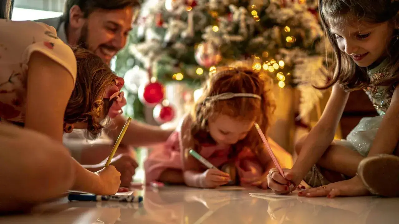 Familia escribiendo cartas a los Reyes Magos junto al &aacute;rbol de Navidad. Quiz&aacute;s una carta de reyes magos para ni&ntilde;os que se portan mal, &iexcl;o para los que se portan bien!