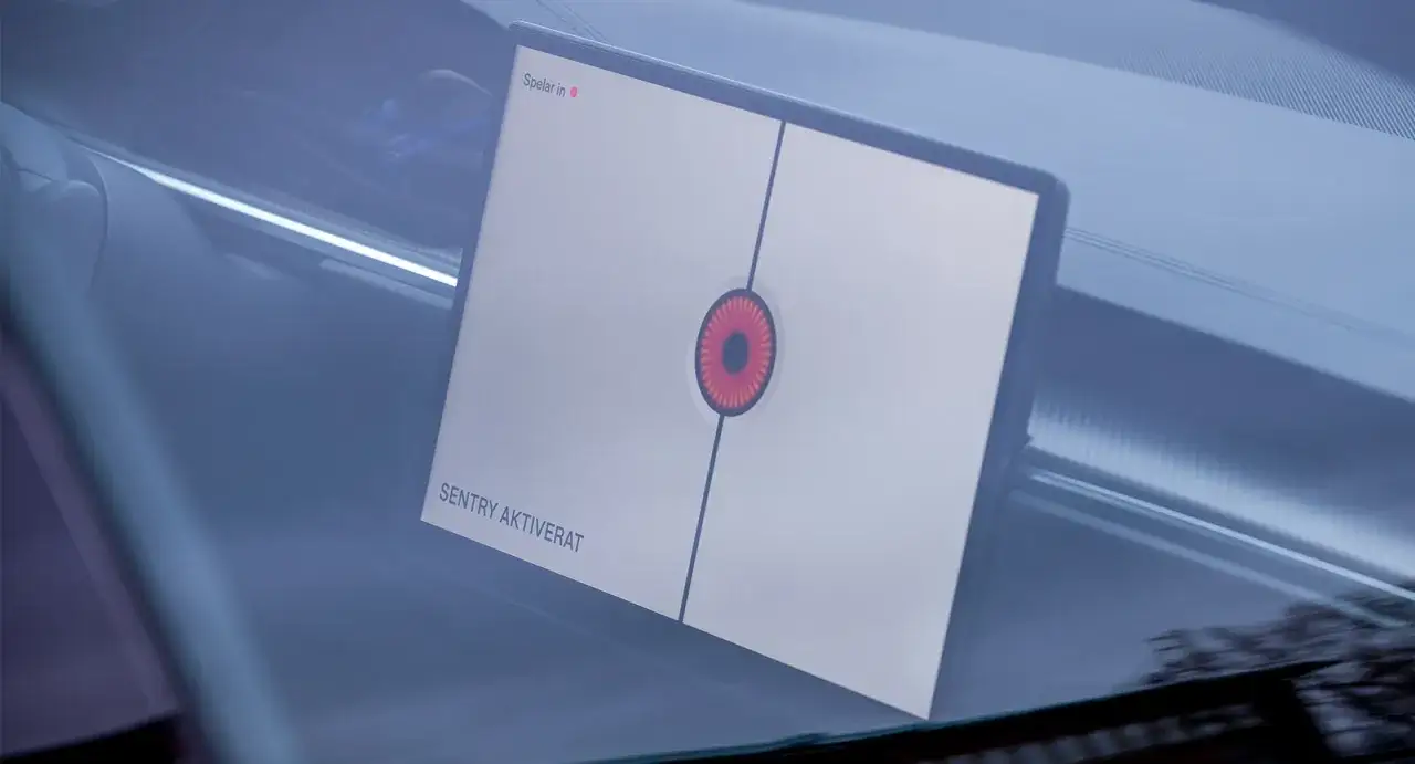 Tesla Sentry Mode aktiverat. En röd ögonliknande symbol visas på skärmen, vilket indikerar att säkerhetsläget är igång.