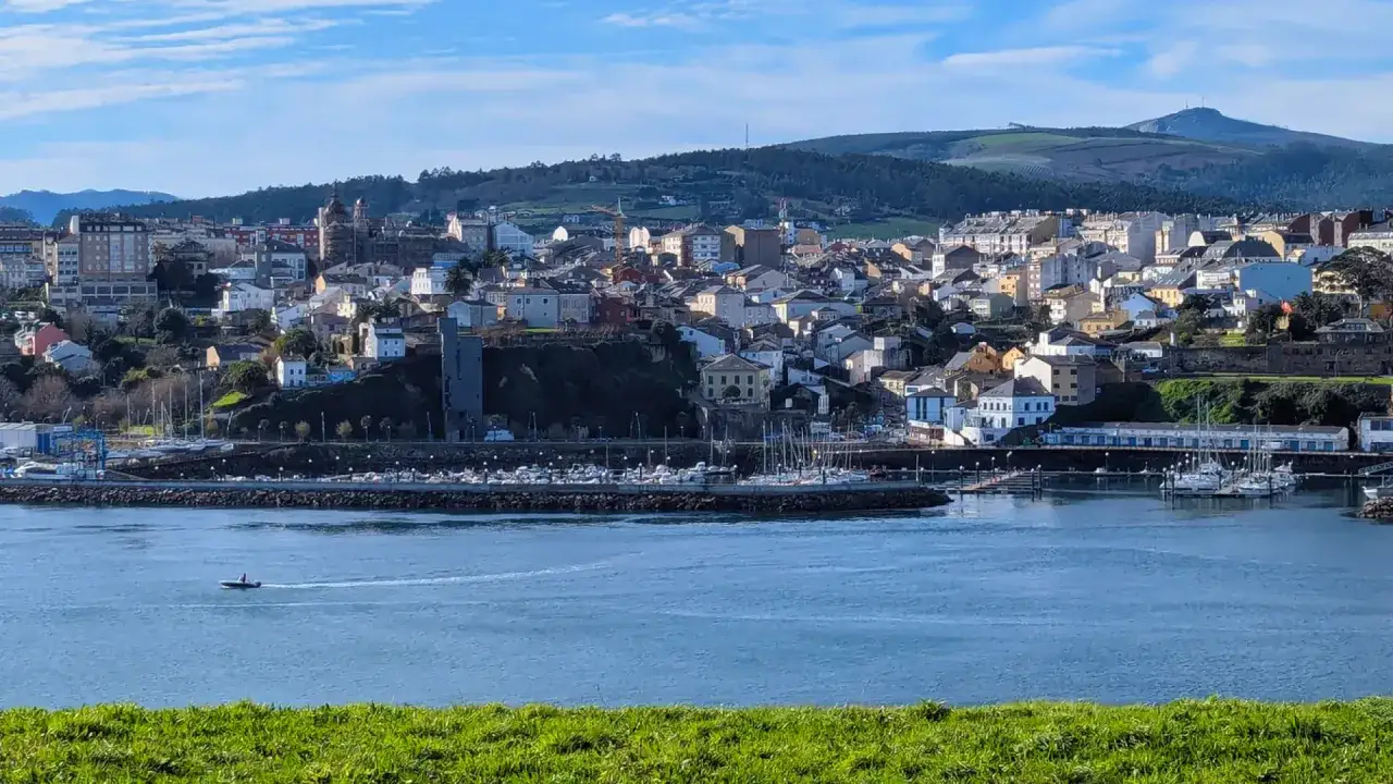 Vista del **mirador Ribadeo** con el puerto deportivo, barcos y la ciudad al fondo bajo un cielo azul.