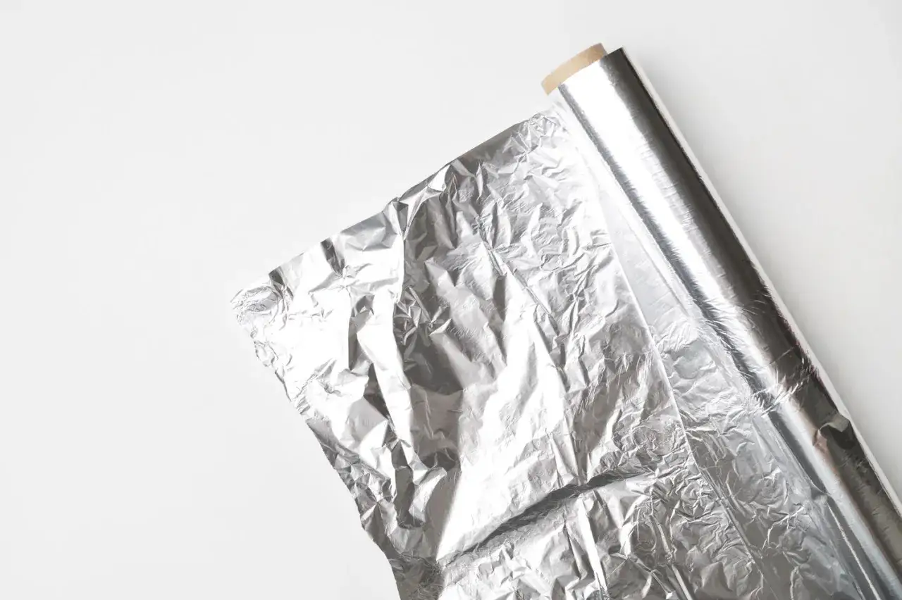 Zrolowana folia aluminiowa na białym tle. Która strona folii utrzymuje ciepło? Ta błyszcząca, która odbija promieniowanie.