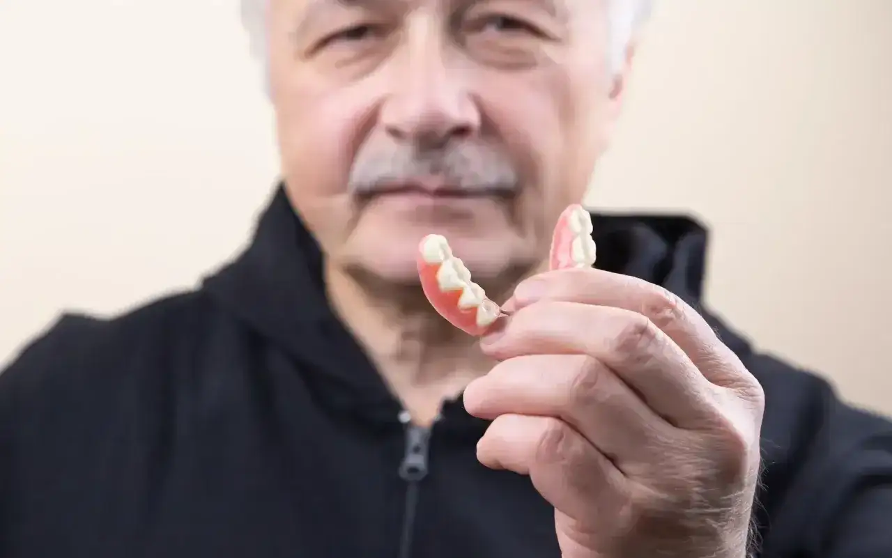 Starszy mężczyzna trzyma protezę. Dowiedz się, jak usunąć klej do protez z dziąseł, aby zapewnić komfort.