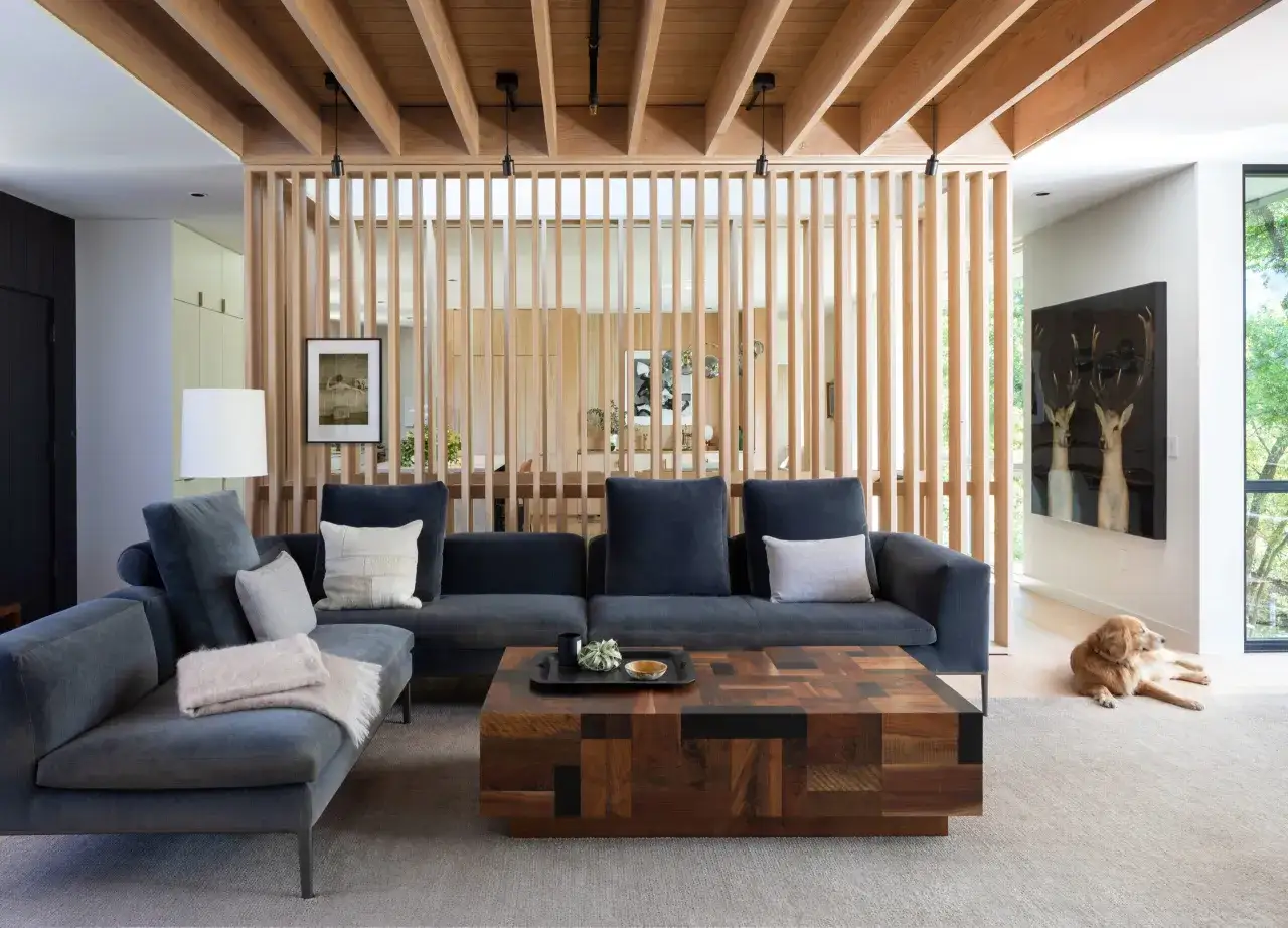 Moderne raumteiler ideen: Ein Holzelement trennt den Wohnbereich mit dunklem Sofa und Holztisch vom Essbereich. Ein Hund liegt entspannt daneben.