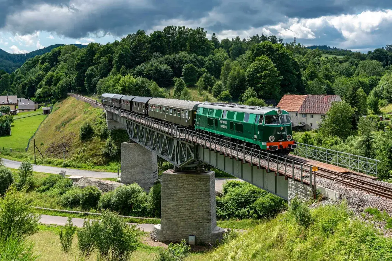 Zielony pociąg PKP SU45-079 jedzie po wiadukcie, pokonując malowniczą trasę, idealną, by zobaczyć, gdzie w góry z Wrocławia pociągiem.