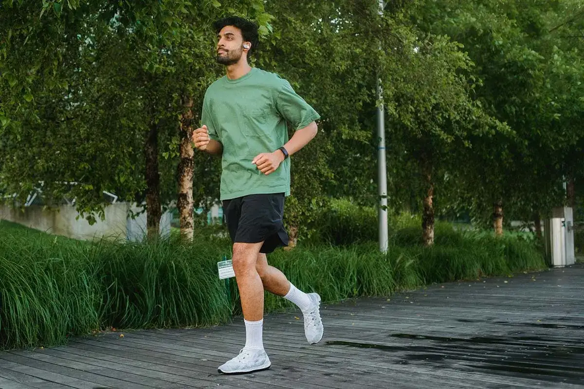 Un homme court sur un sentier en bois, suivant son programme reprise course &agrave; pied. Il porte des &eacute;couteurs et un bracelet d'activit&eacute;.