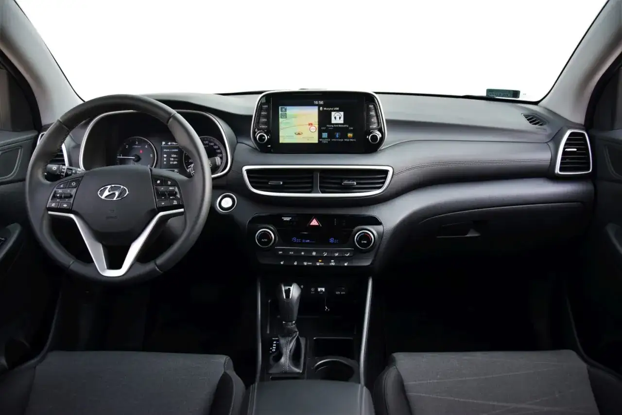 Wnętrze Hyundai Tucson 2025: kierownica, ekran multimedialny z nawigacją, panel klimatyzacji i dźwignia zmiany biegów.