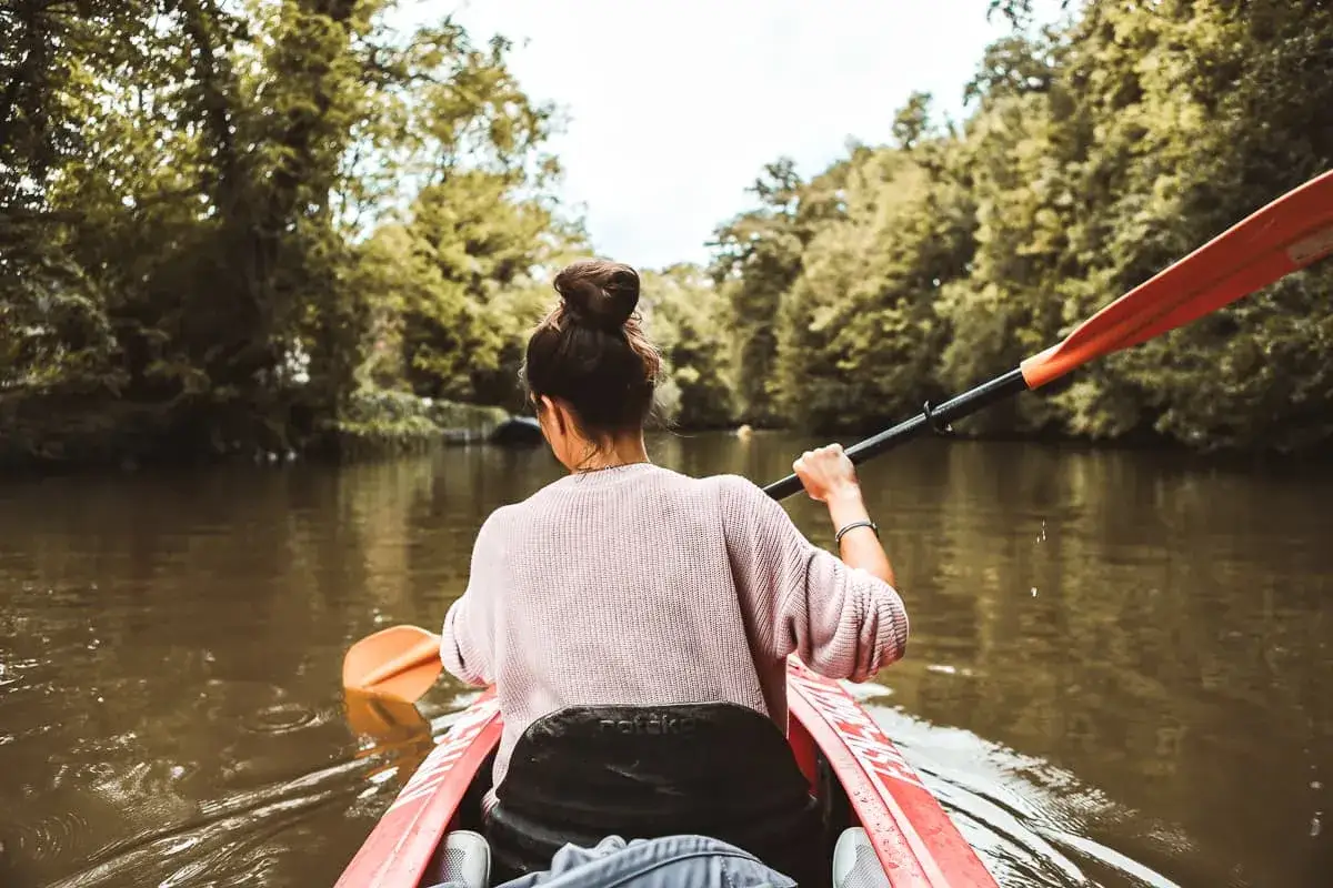 Frau paddelt im Kajak auf einem Fluss, umgeben von gr&uuml;nen B&auml;umen. Ein tolles Erlebnis f&uuml;r Ausflugsziele Sachsen.
