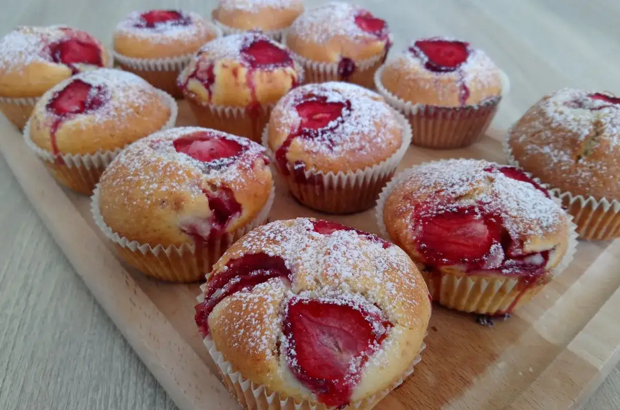 Pyszne muffinki z truskawkami, posypane cukrem pudrem, kuszą swoim wyglądem.