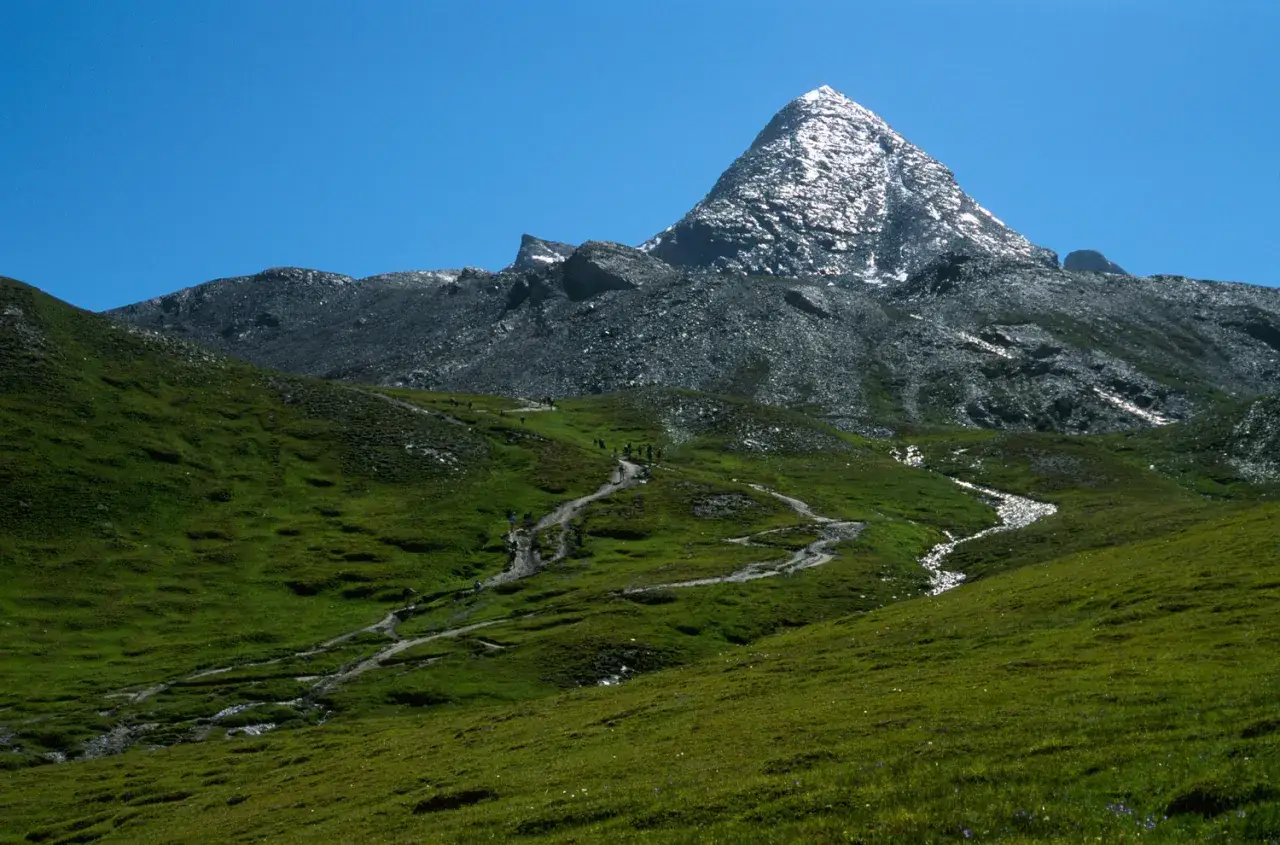 Randonneurs sur un sentier sinueux menant au Pain de Sucre, montagne majestueuse sous un ciel bleu.