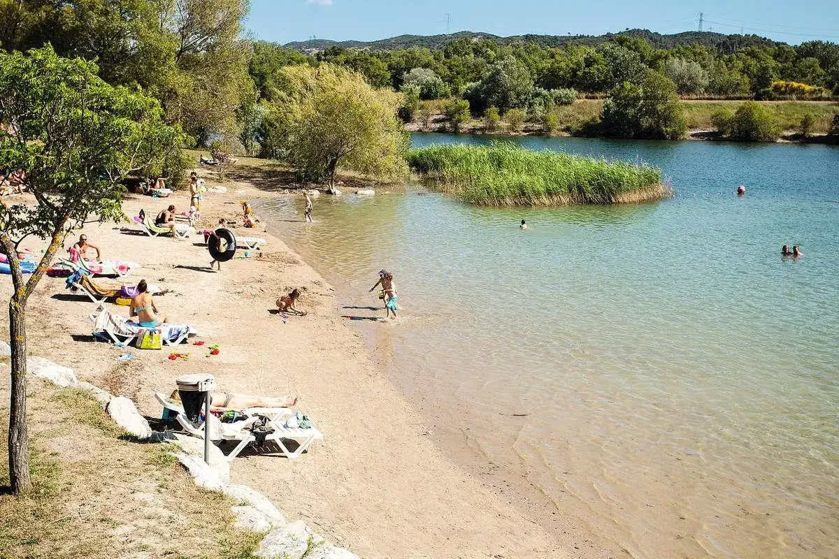 Plage animée à l'étang de la Bonde, des baigneurs profitent du soleil et de l'eau claire, entourés de verdure.