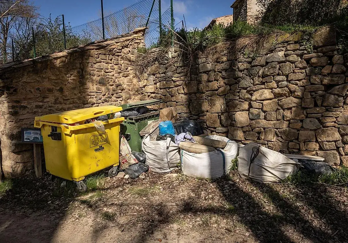 Contenedores de basura desbordados junto a un muro de piedra. &iquest;Qui&eacute;n querr&iacute;a comprar una casa sin luz ni agua en estas condiciones?