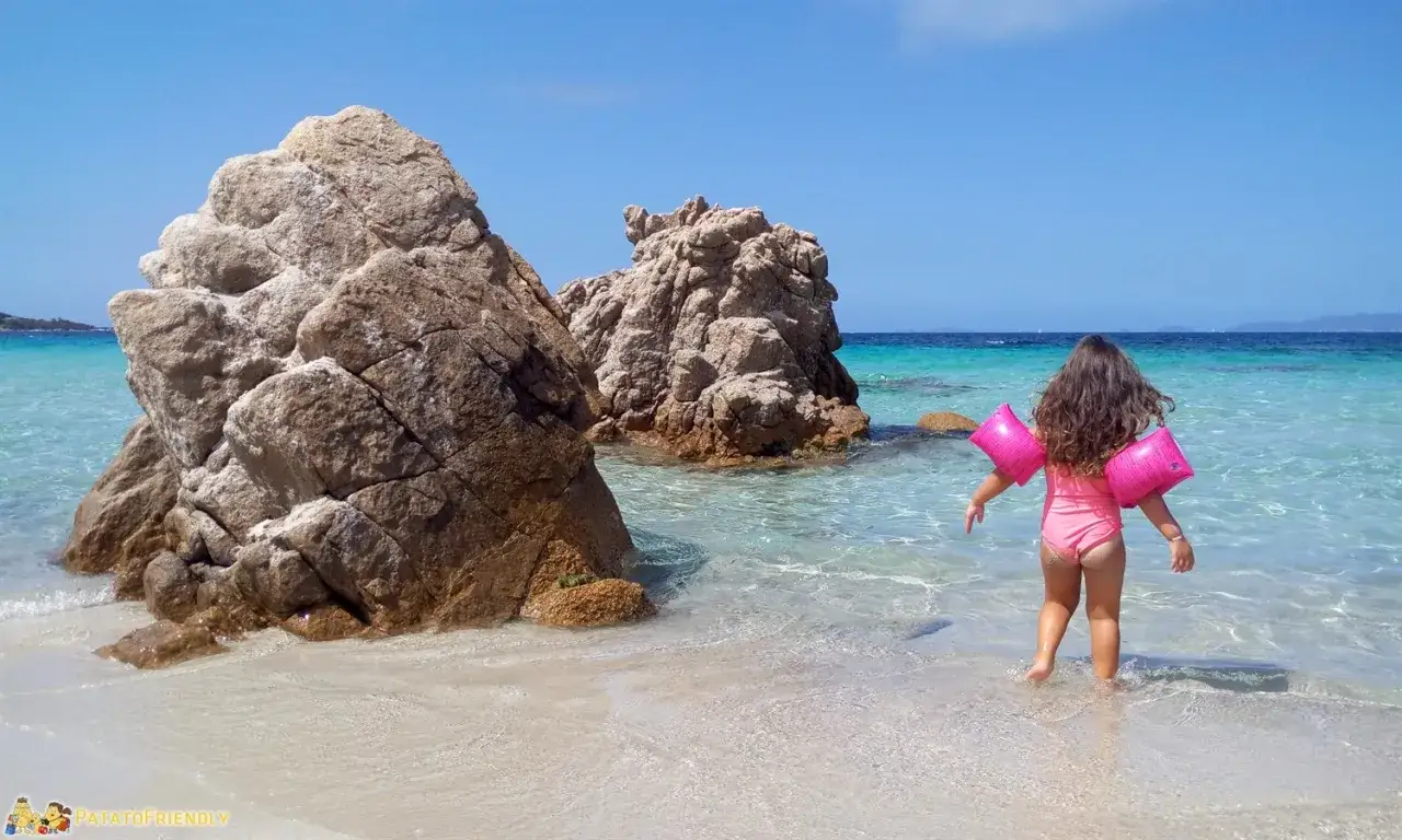Bambina con braccioli rosa esplora le acque cristalline della Corsica, tra scogli imponenti e sabbia bianca. Vacanze indimenticabili in Corsica con bambini.