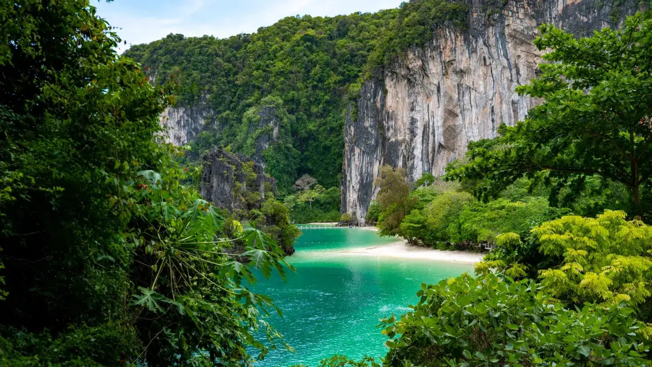 T&uuml;rkisblaue Bucht mit Sandstrand, umrahmt von steilen, bewachsenen Felsen. Perfekt f&uuml;r die beste Reisezeit Thailand.