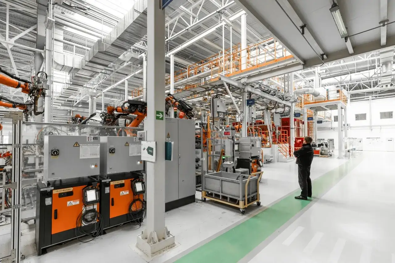 Robotyczne ramiona wstrzymane, pracownik obserwuje przestój. Skutki przerwania dostaw energii elektrycznej do urządzeń o kluczowym znaczeniu.