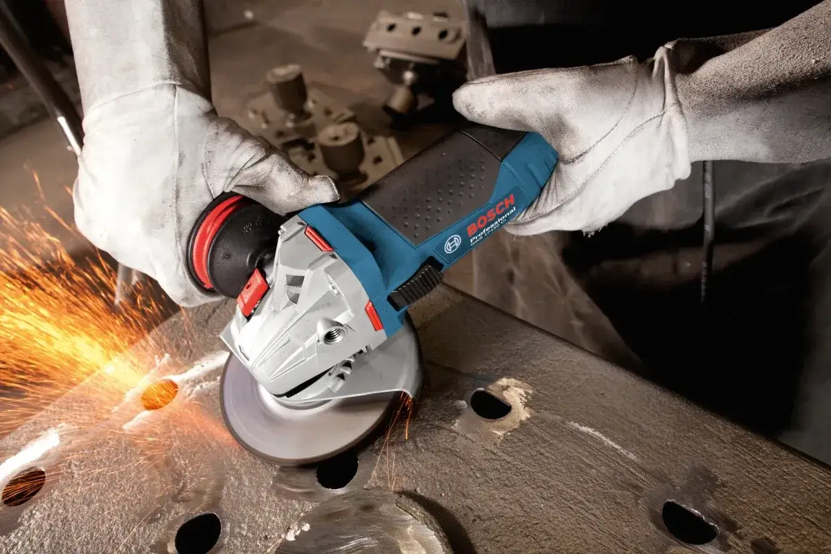 Ręce w rękawicach trzymają szlifierkę kątową Bosch, której dysk do szlifierki kątowej iskrzy podczas pracy z metalem.