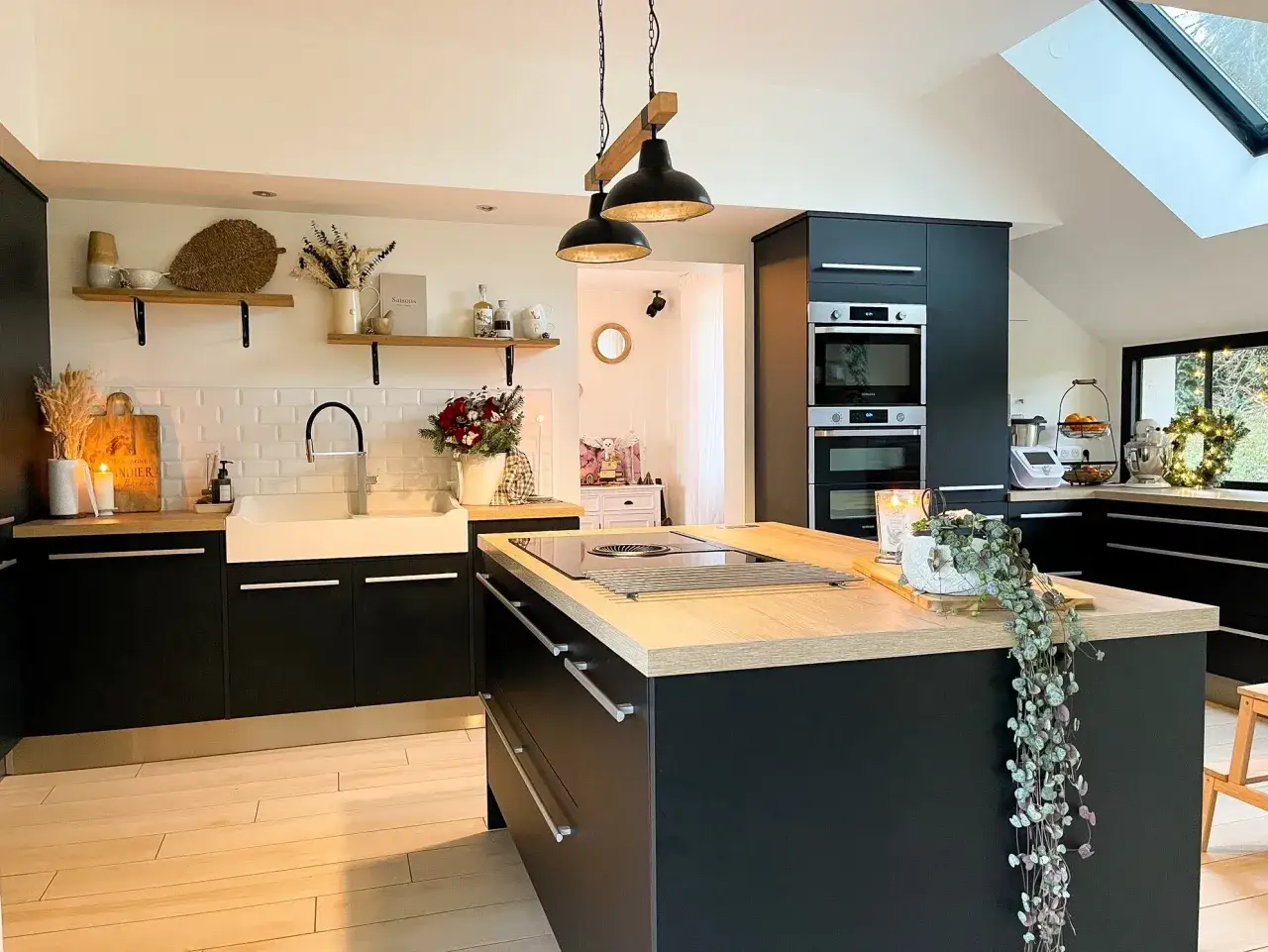Cuisine moderne et chaleureuse, idéale pour la création culinaire. Évier blanc, îlot central en bois, et rangements noirs.