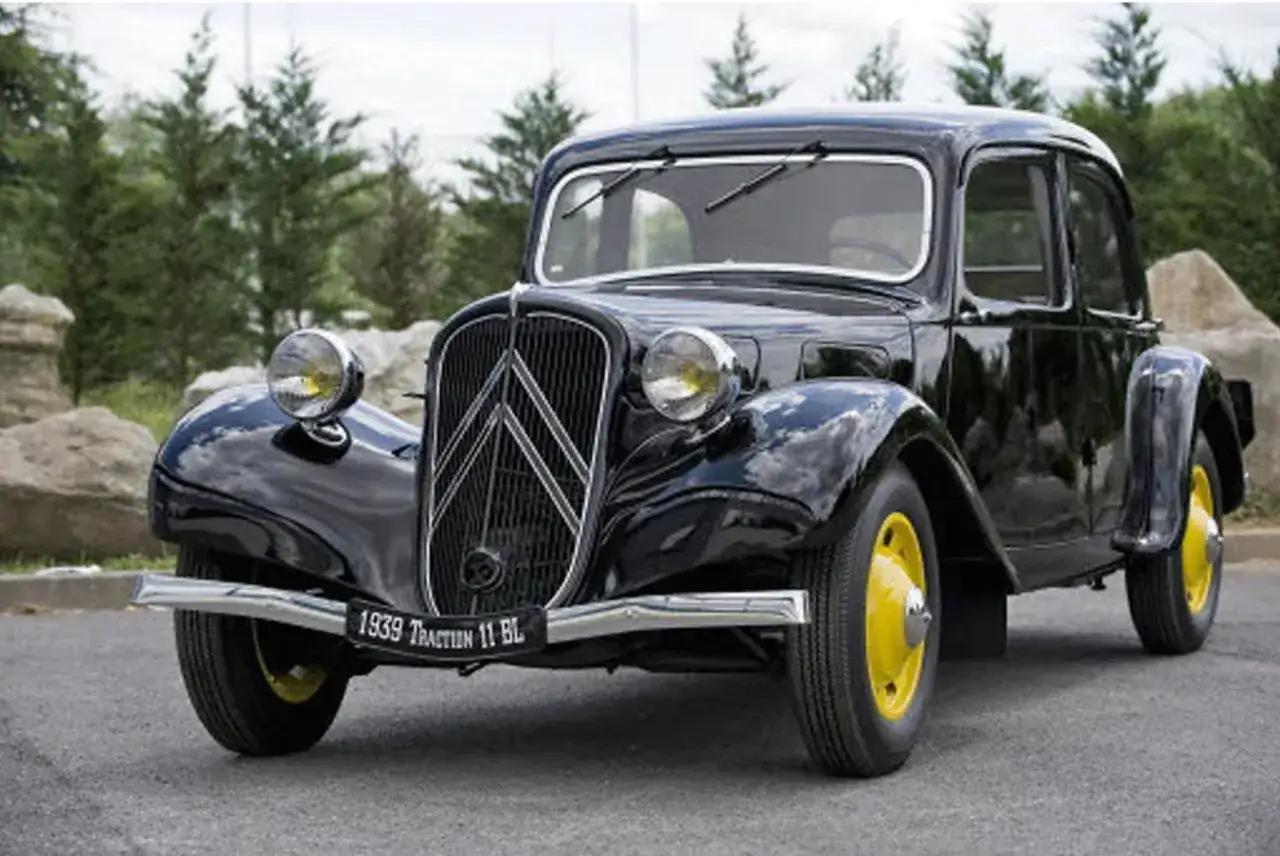 Czarny, zabytkowy samochód po francusku, model z 1939 roku, z żółtymi felgami, na tle drzew i skał.