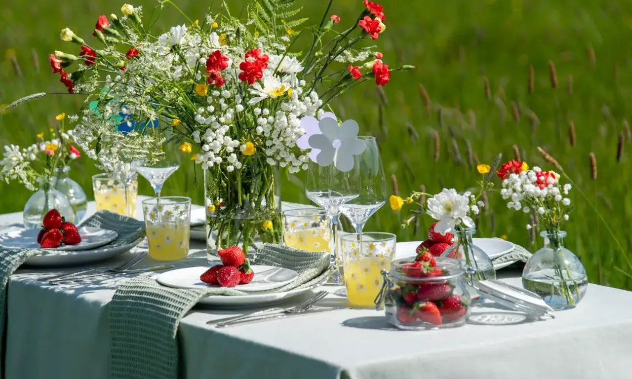 En vackert dukad picknick med färska jordgubbar och vilda blommor. Perfekt för en sommarfest utomhus, med blommor till dukning som skapar en härlig atmosfär.