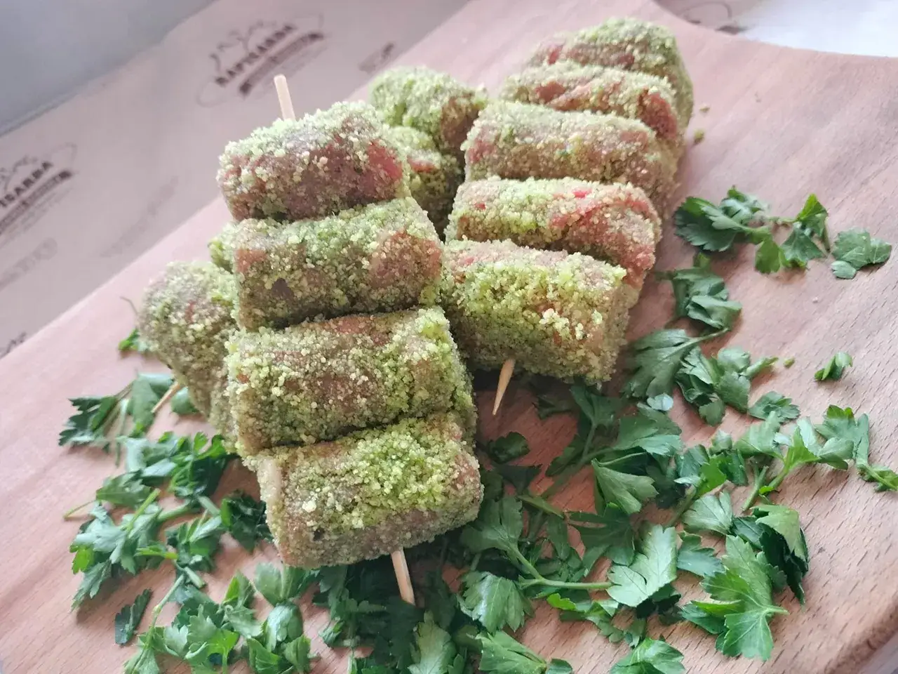 Involtini di carne su spiedini, impanati con erbe verdi e prezzemolo fresco, pronti per essere cucinati.