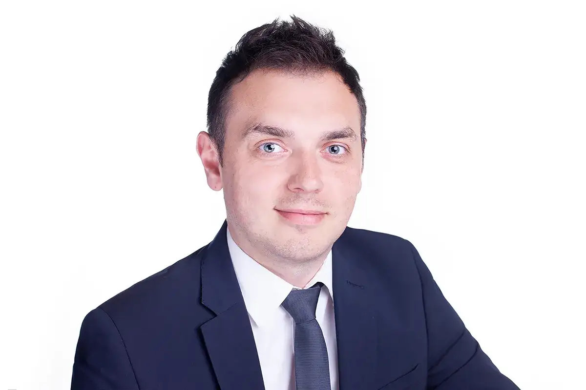 Portret mężczyzny w garniturze i krawacie, z jasnymi oczami, na białym tle.