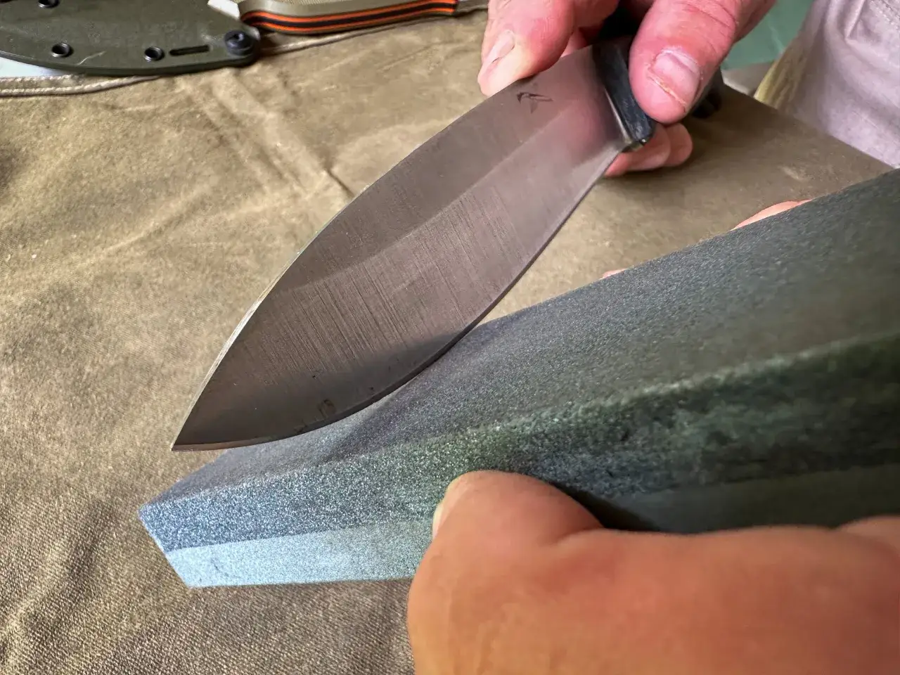 H&auml;nder slipar en kniv med en slipsten. En knivs egg blir vass igen.