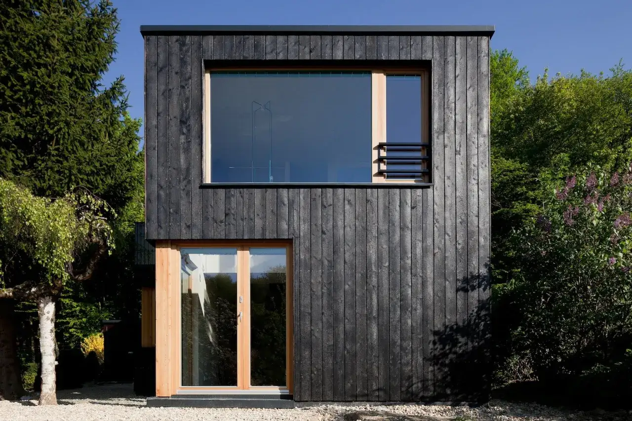 Moderne Architektur mit dunklen Holzfassaden, großen Fenstern und Holztüren. Ein Beispiel für ansprechende Holzfassaden in natürlicher Umgebung.