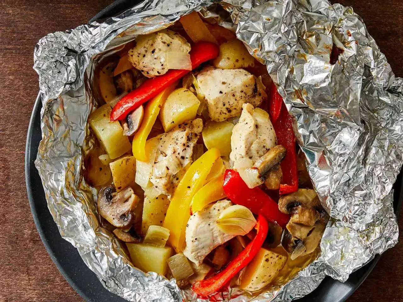 A delicious meal of chicken, potatoes, peppers, and mushrooms cooked in foil packets. This shows how to make foil packets for an easy, flavorful dish.