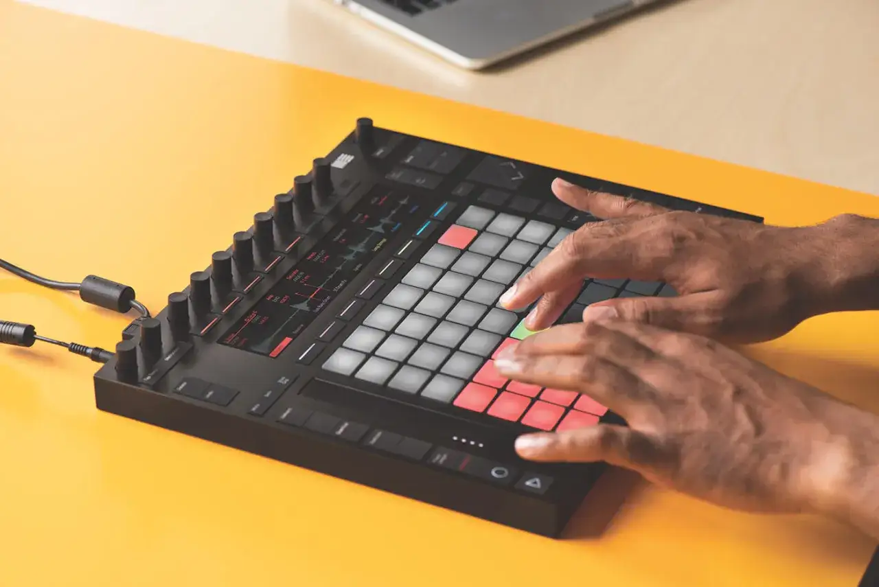 Mains jouant sur un contr&ocirc;leur pour un tuto Ableton Live 11. Les pads lumineux cr&eacute;ent une ambiance cr&eacute;ative.