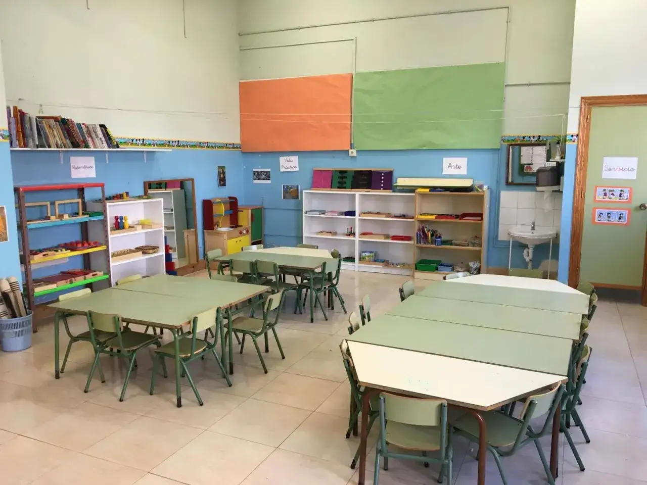 Aula preparada con mesas y sillas para el m&eacute;todo Montessori en colegios. Estanter&iacute;as con materiales did&aacute;cticos y zonas de 