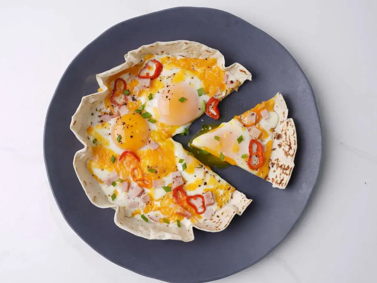 Pyszna pizza na tortilli z jajkami sadzonymi, serem, szynką i papryczką chili.