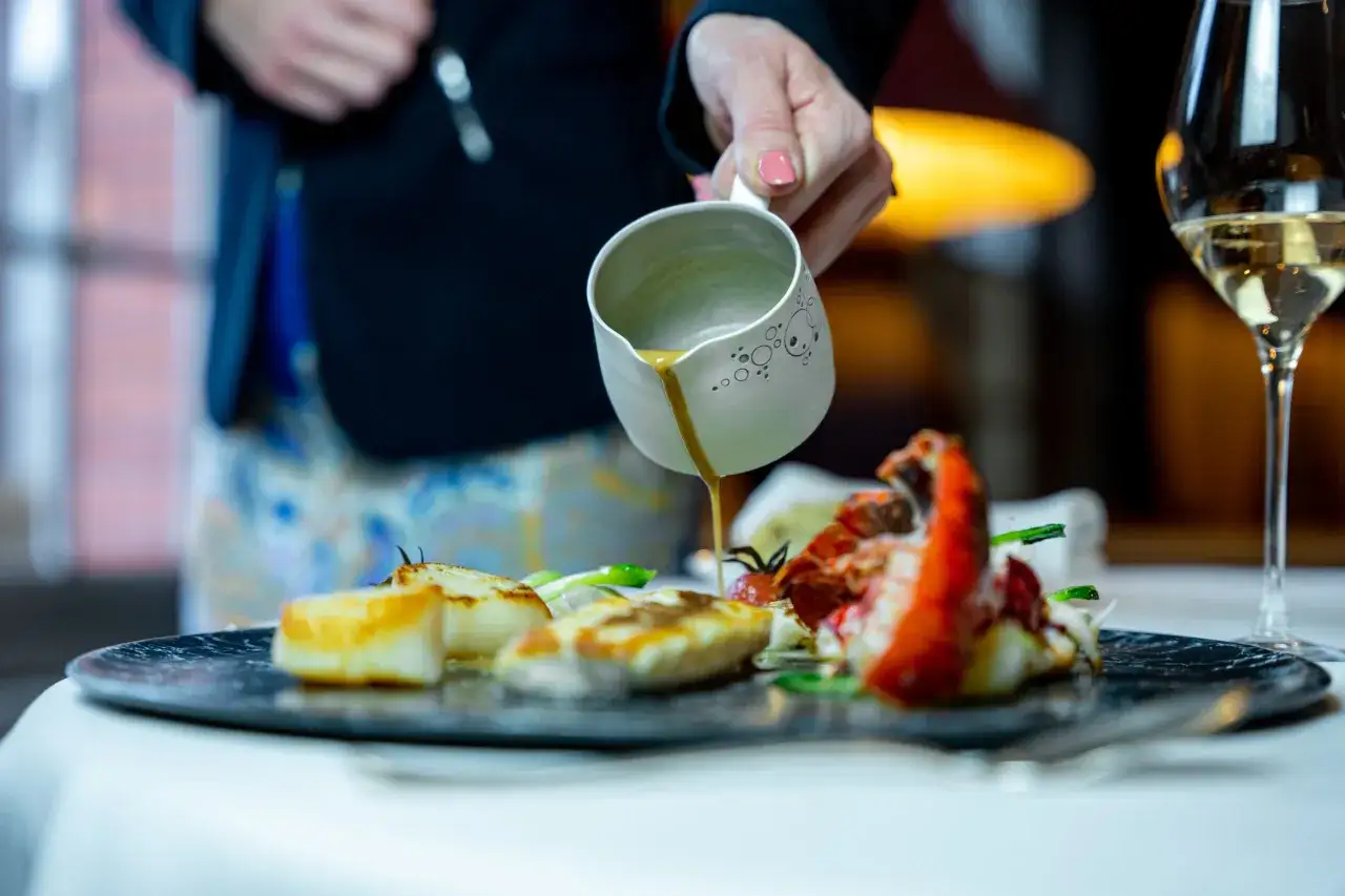 Un chef verse une sauce sur un plat de fruits de mer, avec un verre de cr&eacute;mant &agrave; c&ocirc;t&eacute;. Quel est le meilleur cr&eacute;mant pour accompagner ce d&eacute;lice ?