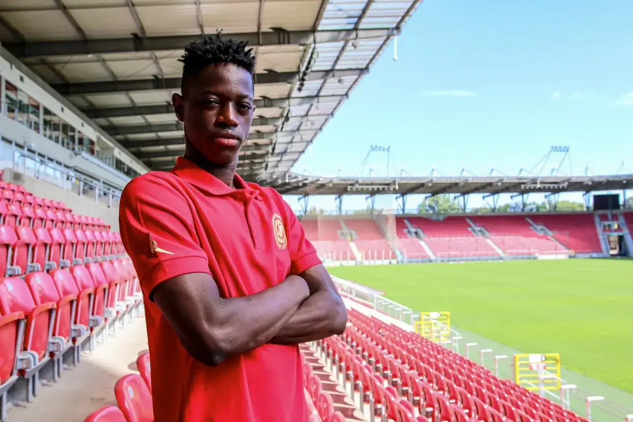 Młody piłkarz w czerwonej koszulce z herbem klubu, na tle pustych trybun stadionu. Czy to nowy nabytek, o którym krążą plotki transferowe Widzew?